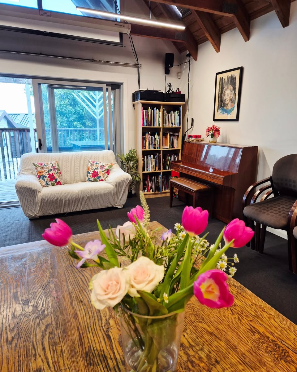 The library room at 788 with a sofa, piano, bookshelves, flowers and a framed portrait of Raye Freedman