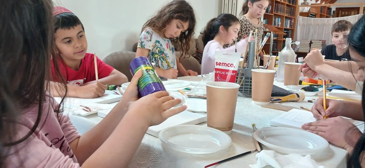 Children painting at a long table surrounded by library bookshelves