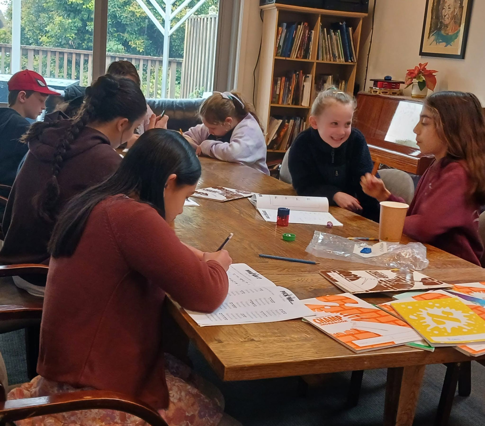 Children and teenagers working through Hebrew School workbooks around a large wooden table